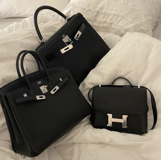 Black Hermes Birkin, Kelly, and Constance bags on white bedding